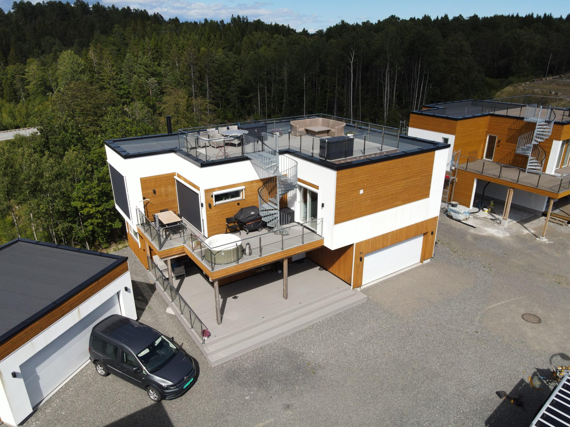 Funkishus i hvitt og tre med takterrasse og garasje, sett fra drone