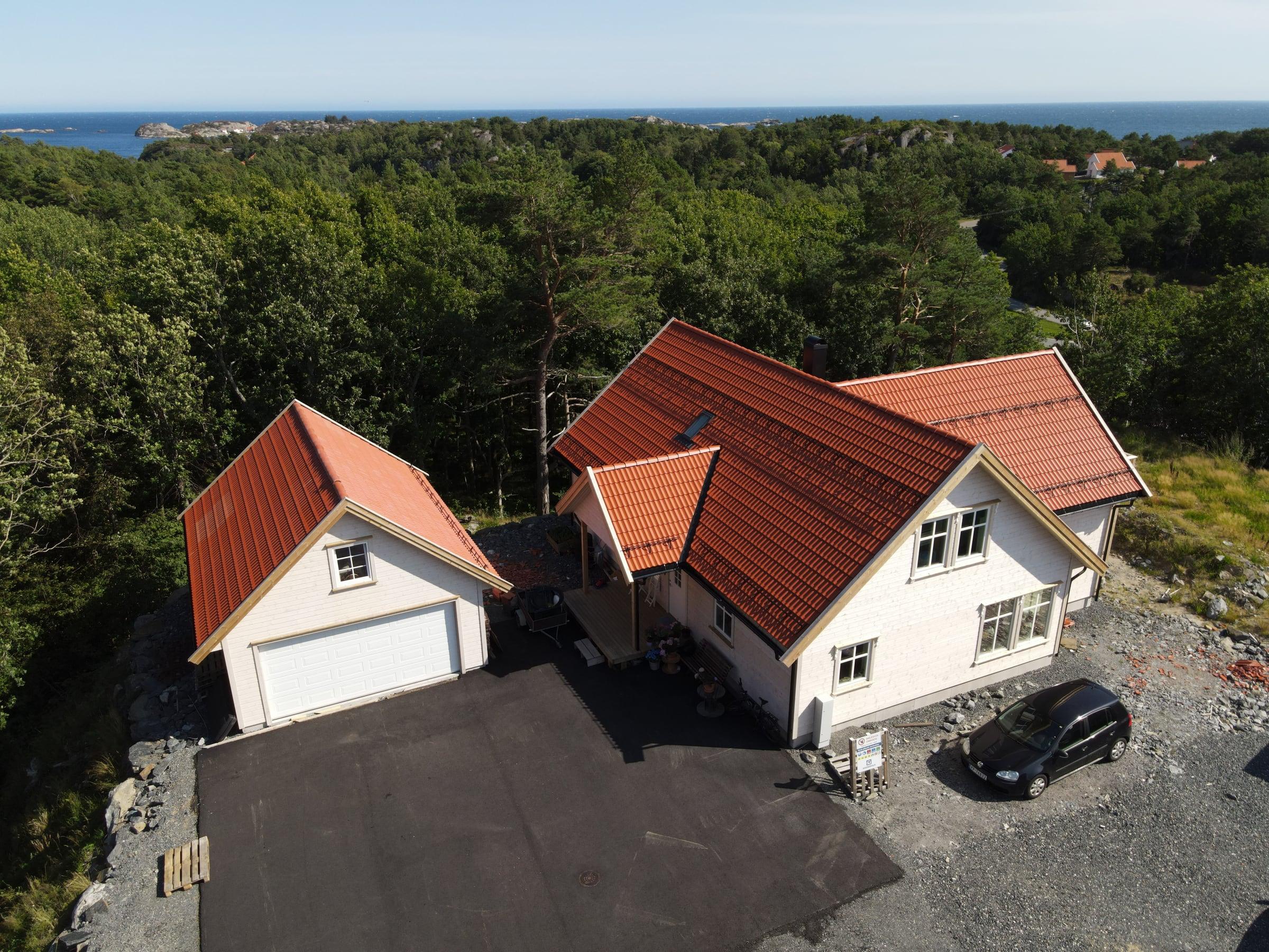 Hvitt hus med oransje teglstein og dobbel garasje, sett fra drone