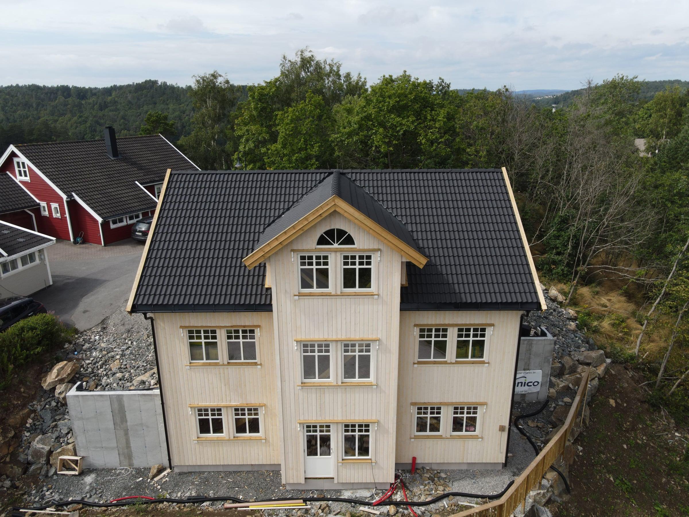 Stort, gult hus i klassisk stil med sort tak, sett fra drone