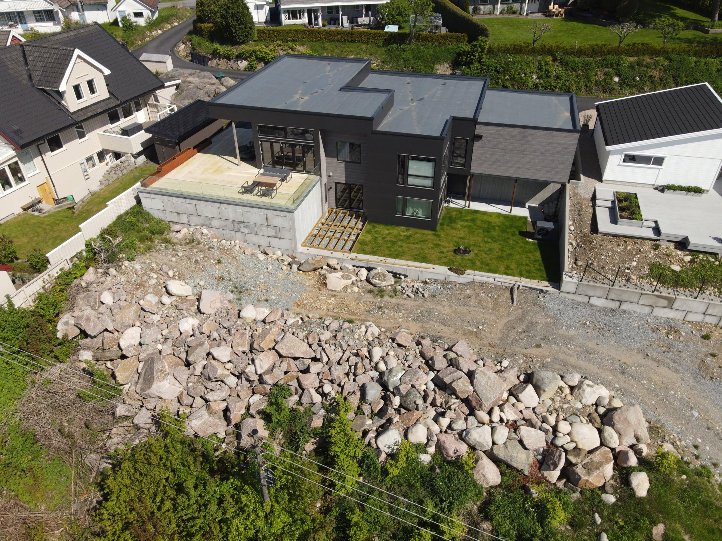 Moderne hus i mørk kledning på en nysprengt tomt med stein, sett fra drone