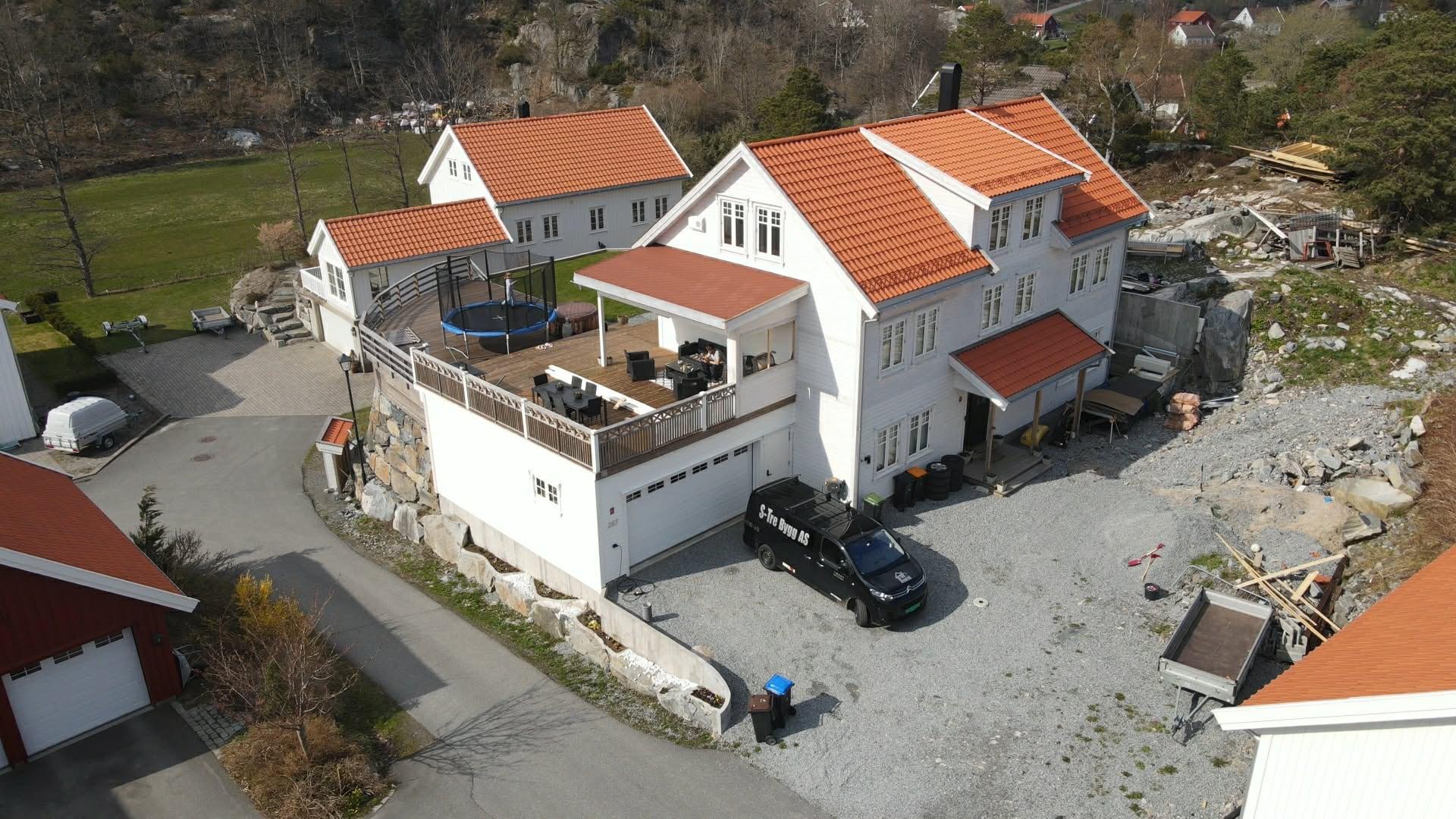 Hvitt hus med oransje teglstein, stor terrasse og garasje, sett fra drone